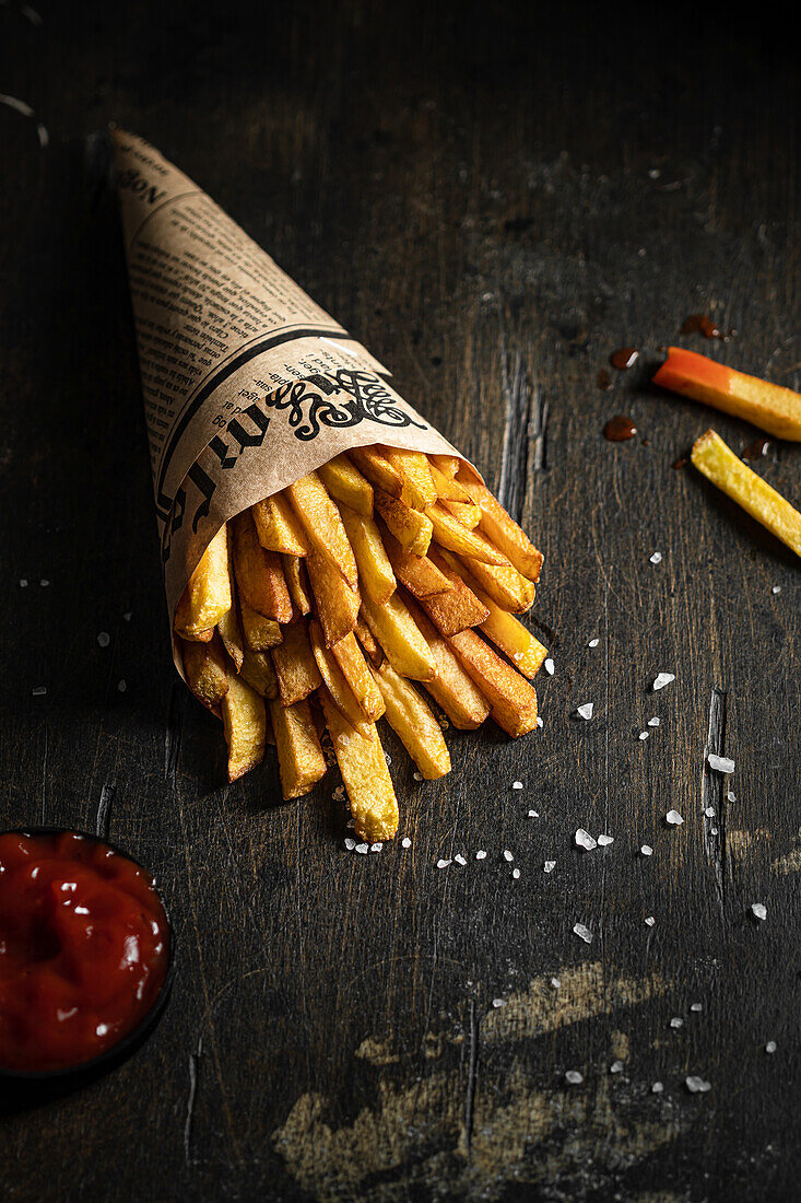 Pommes frites in einer Papiertüte mit Streusalz und Ketchup