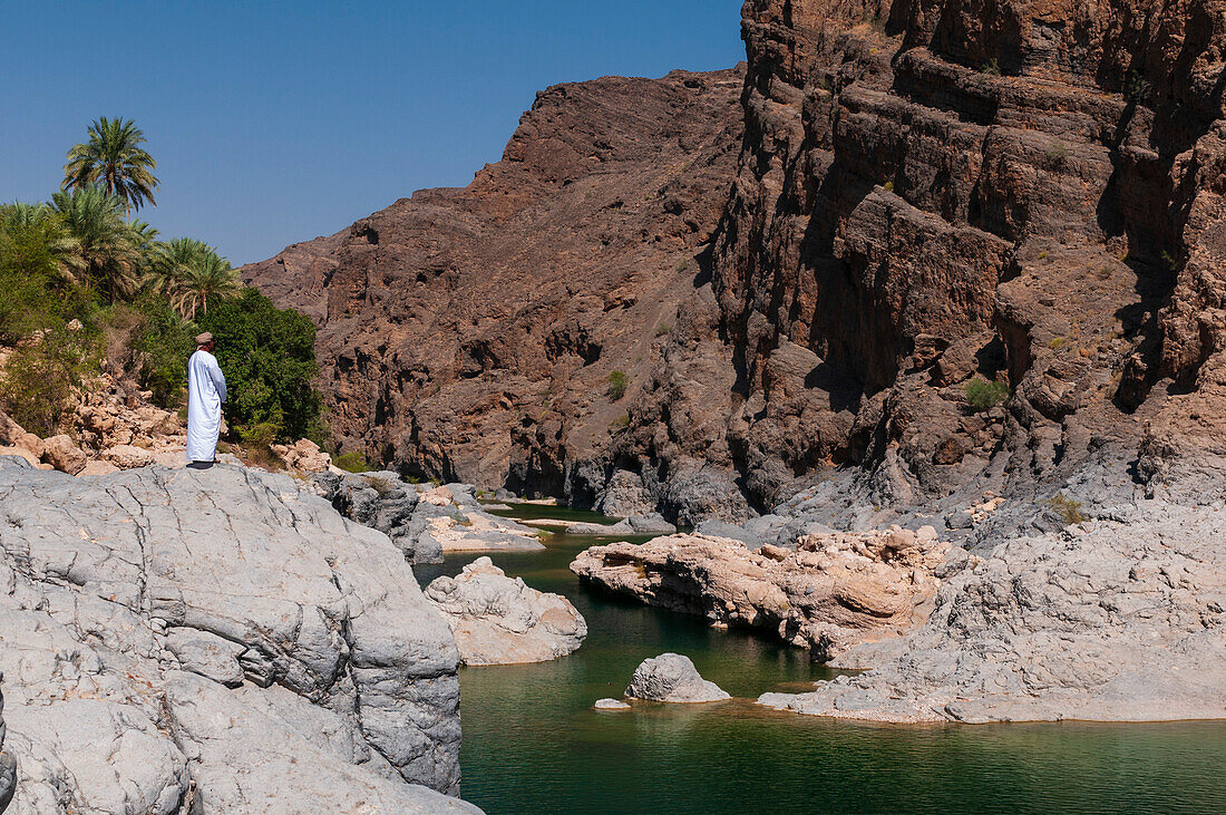 Man looking out over a natural pool, Wadi Al Arbeieen, Oman