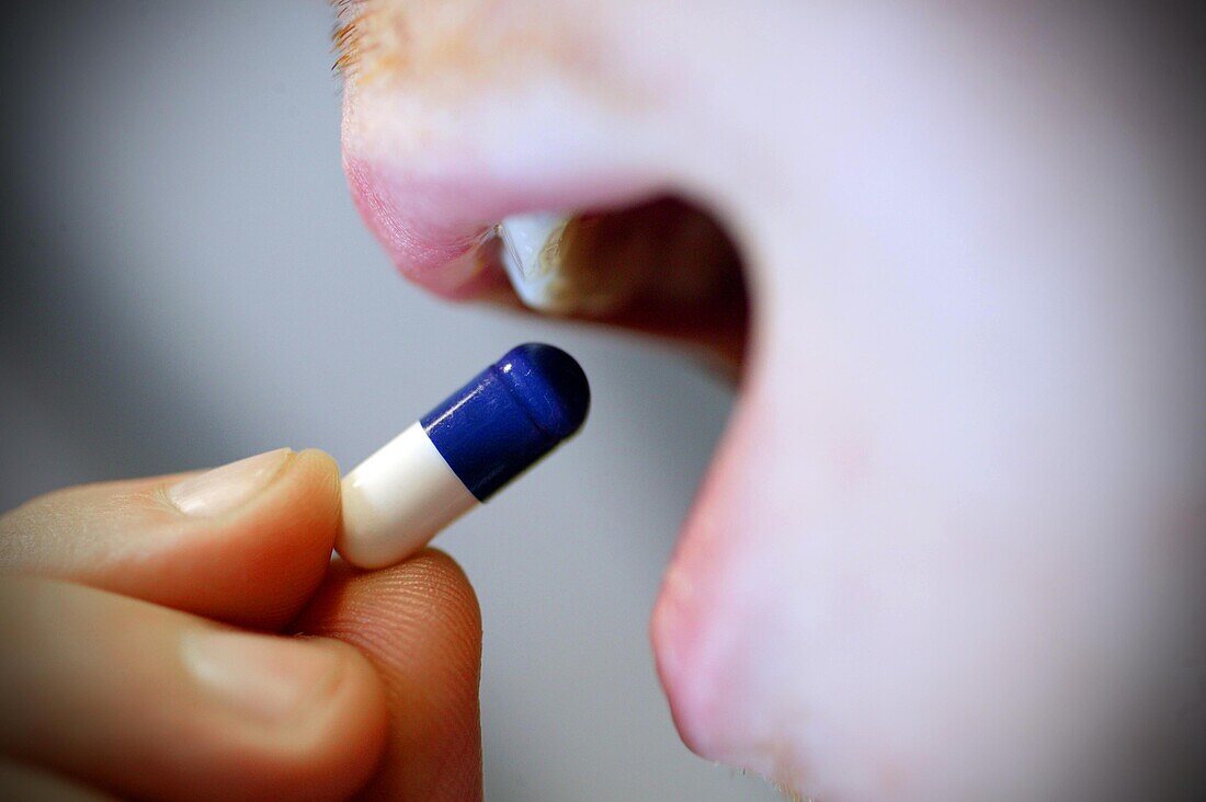 Man putting a blue and white pill into his mouth