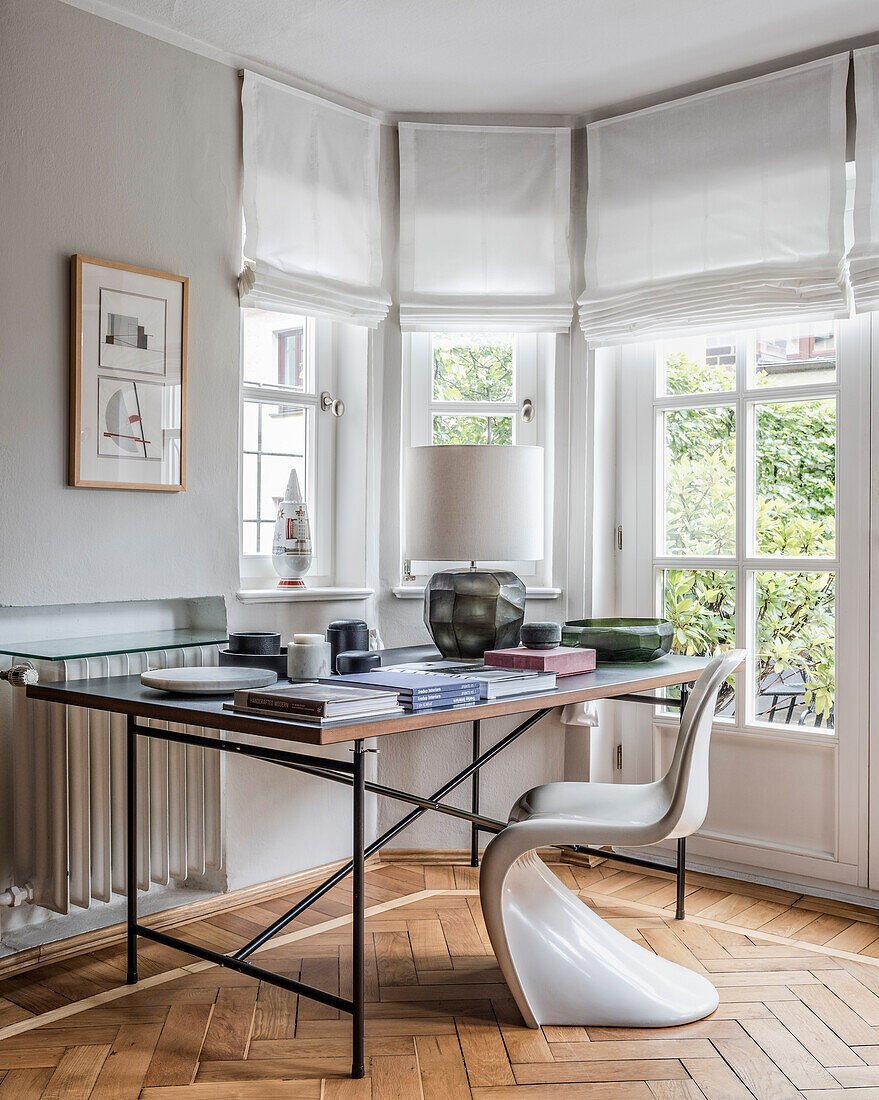 Klassikerstuhl am Schreibtisch mit Büchern und Tischlampe vor Fenster