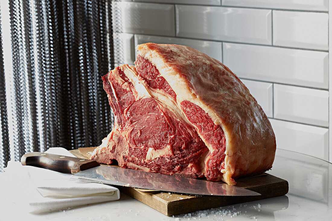 A forerib of beef on the butchers block with a knife