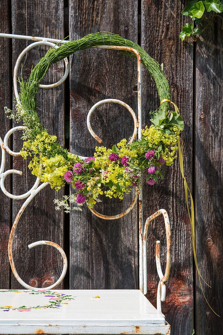 Wreath of fresh flowers on garden bench in front of rustic wooden wall