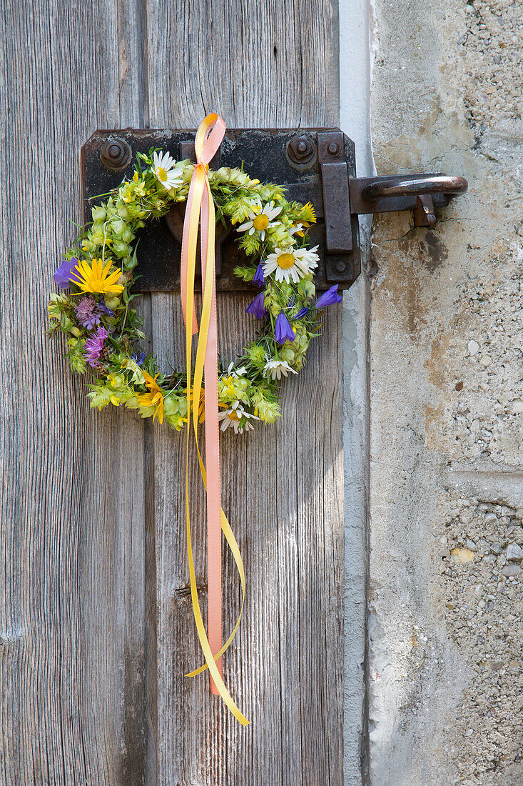 Floral wreath attached to old wooden door with colourful ribbons