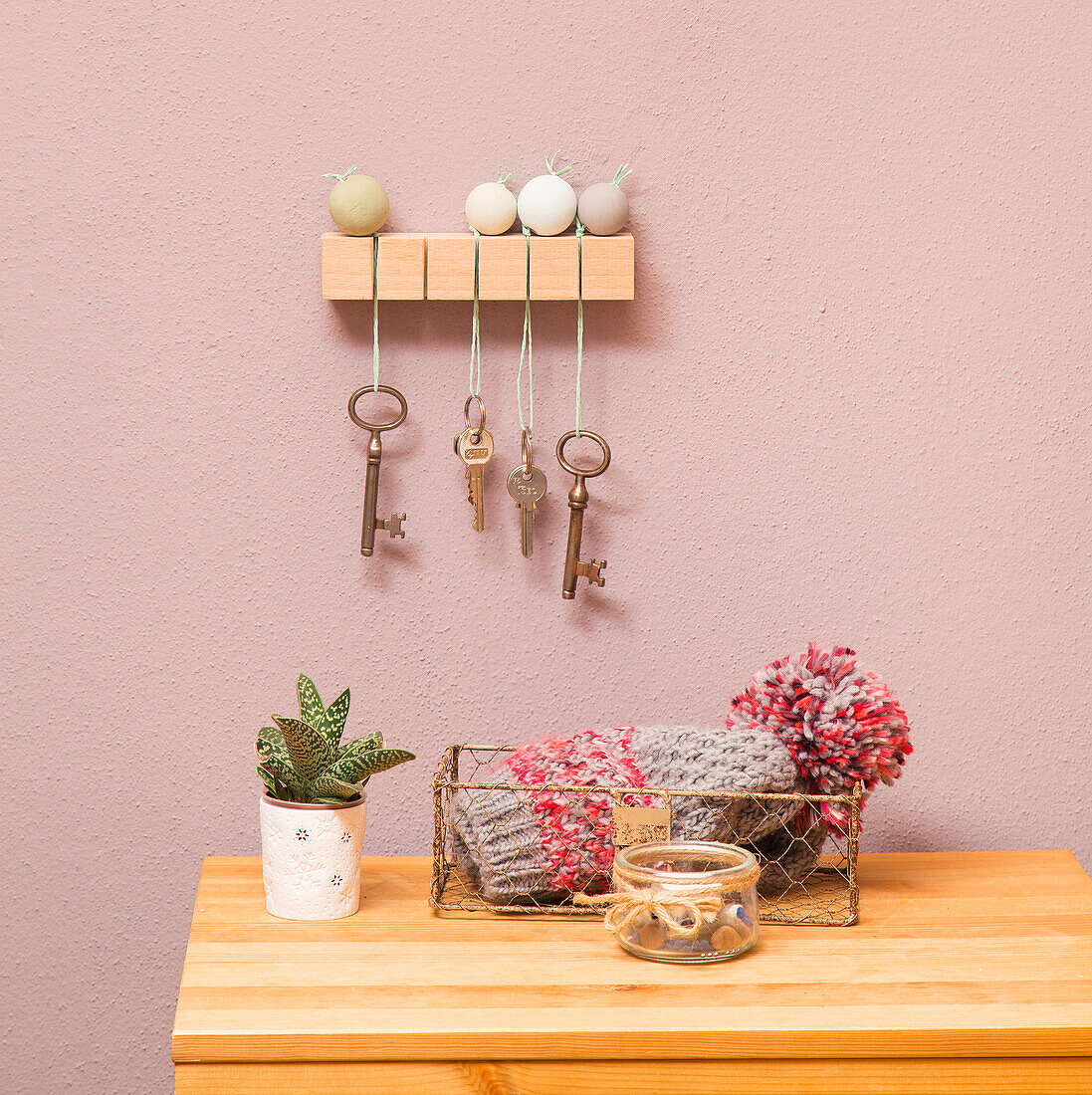 DIY key board on a pink wall above decorations on a wooden chest of drawers