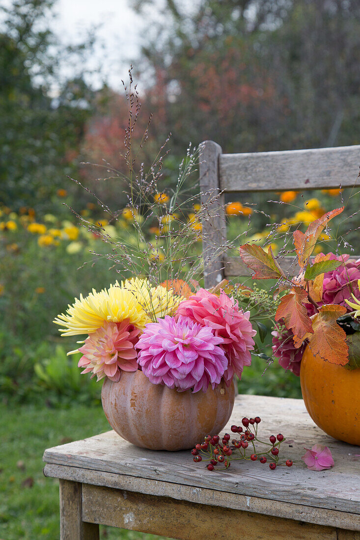 Autumn bouquet of flowers in pumpkin vase on wooden table in the garden