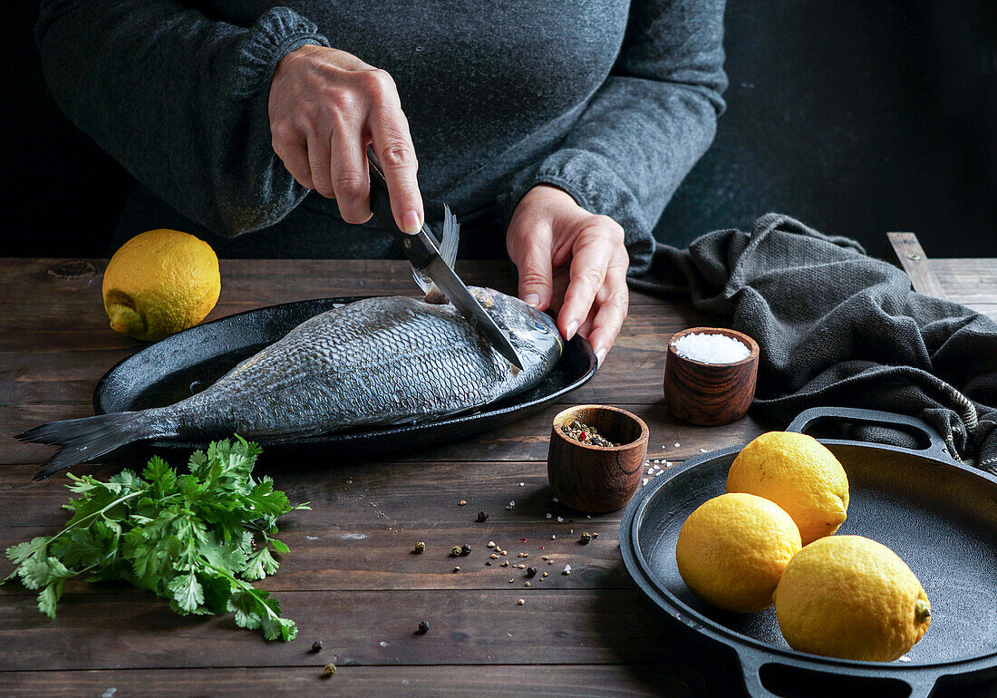 Woman chef preparing a fresh fish dorado by cutting