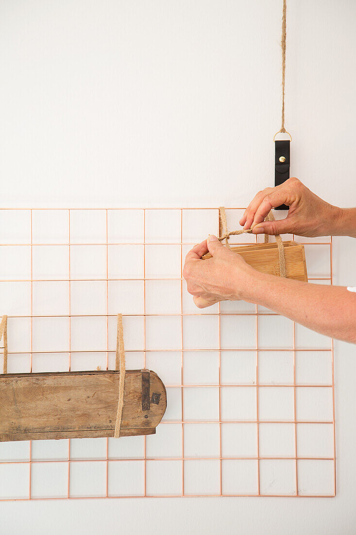 Hände befestigen Holzkistchen an Metallgitter an weißer Wand