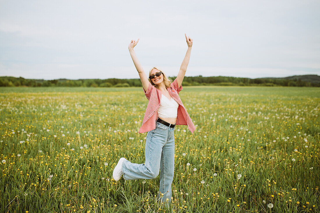 Glückliche junge Frau zeigt Rock-Zeichen auf einer sommerlichen Blumenwiese