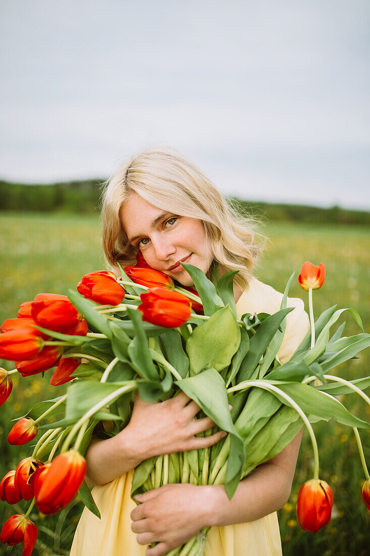 Content female in dress standing with bunch of red tulip flowers in meadow in summer