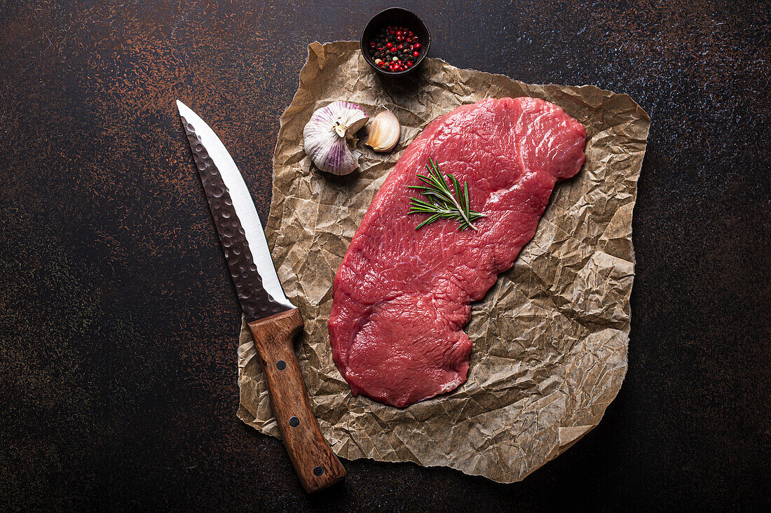 Beef lean raw fillet steak on baking paper with rosemary, garlic and spices
