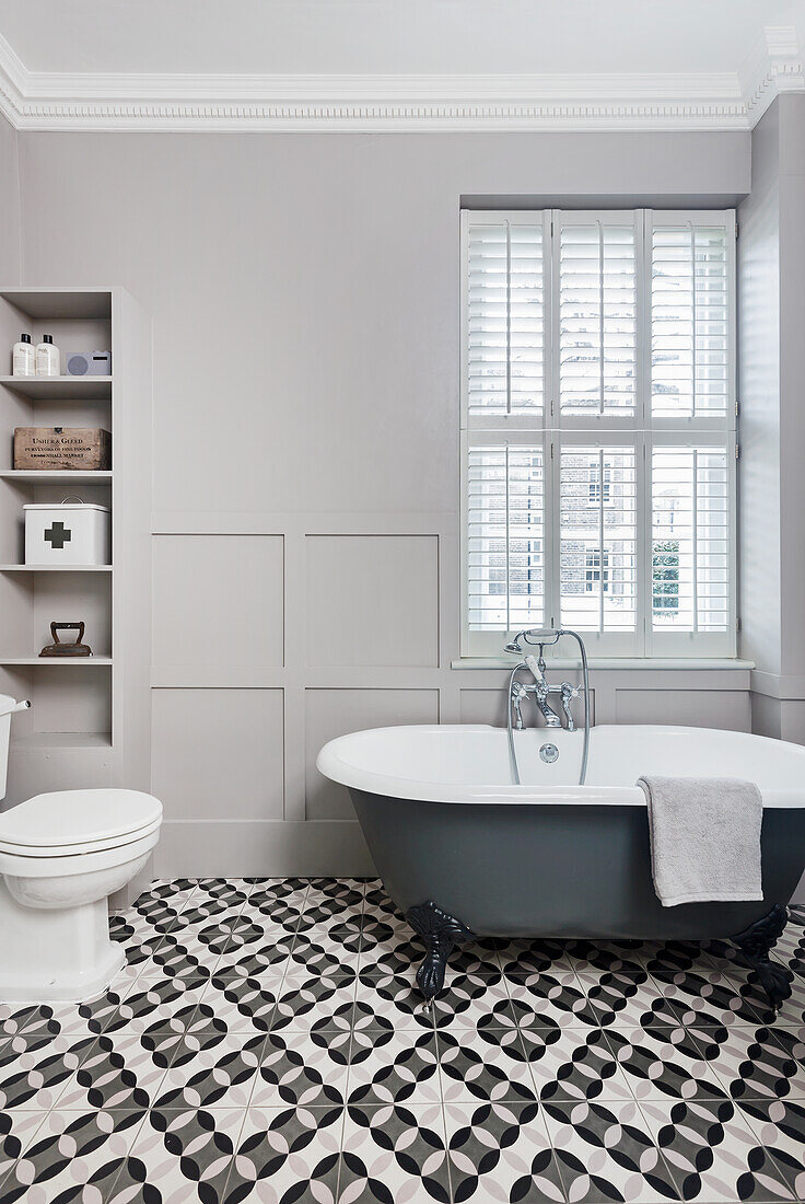 Freestanding bath below window in bathroom with patterned tiled floor