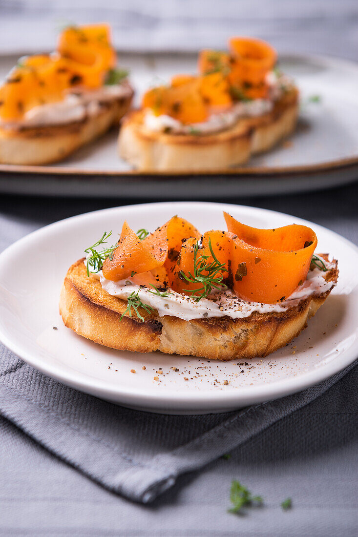 Grilled baguette slices with almond cream, vegan carrot salmon and dill