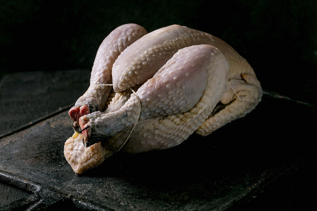 Gerupftes, schwarzes Huhn auf schwarzem Holztisch