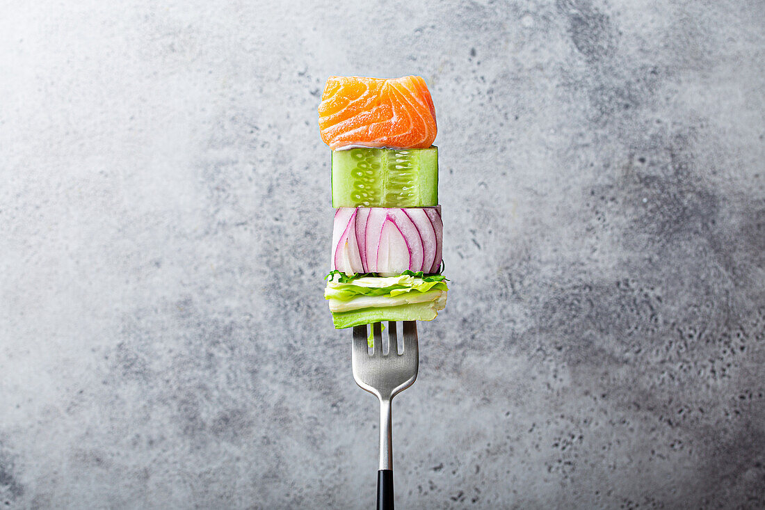 Close-up of fork with food on it: salmon, cucumber, onion, green salad