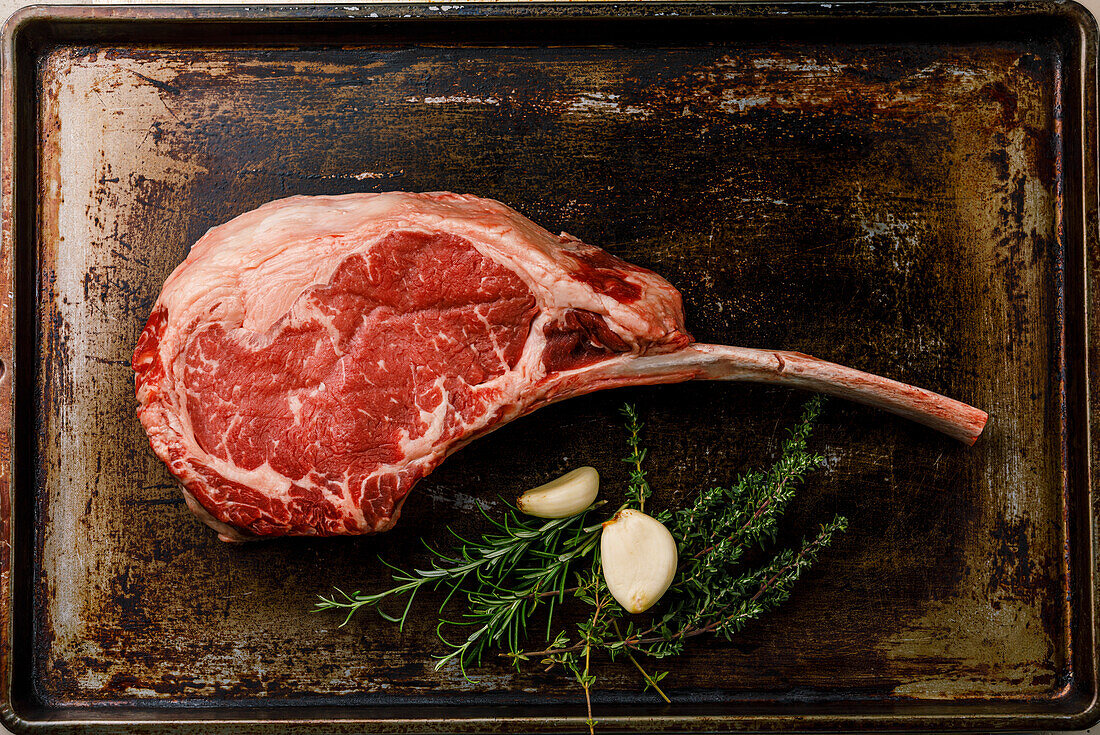 Raw fresh meat Tomahawk Steak and seasonings on dark baking sheet background