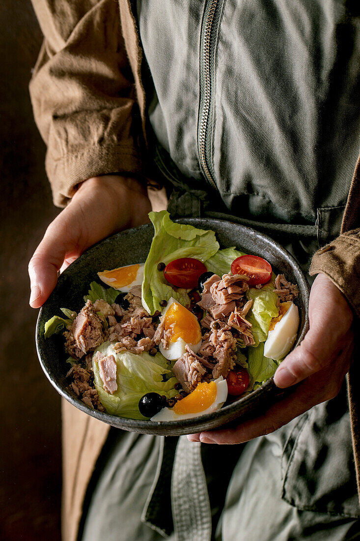 Hände halten Schüssel mit Nizza-Salat mit Dosenthunfisch, Oliven und Eiern