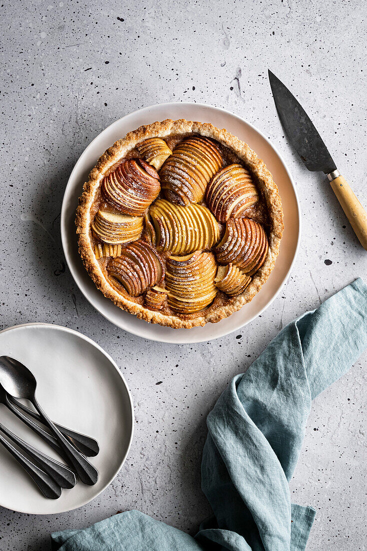 A baked apple tart with serving plates and a knife