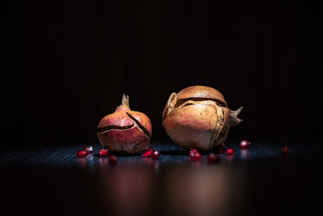 Overripe half peeled pomegranates placed on dark background