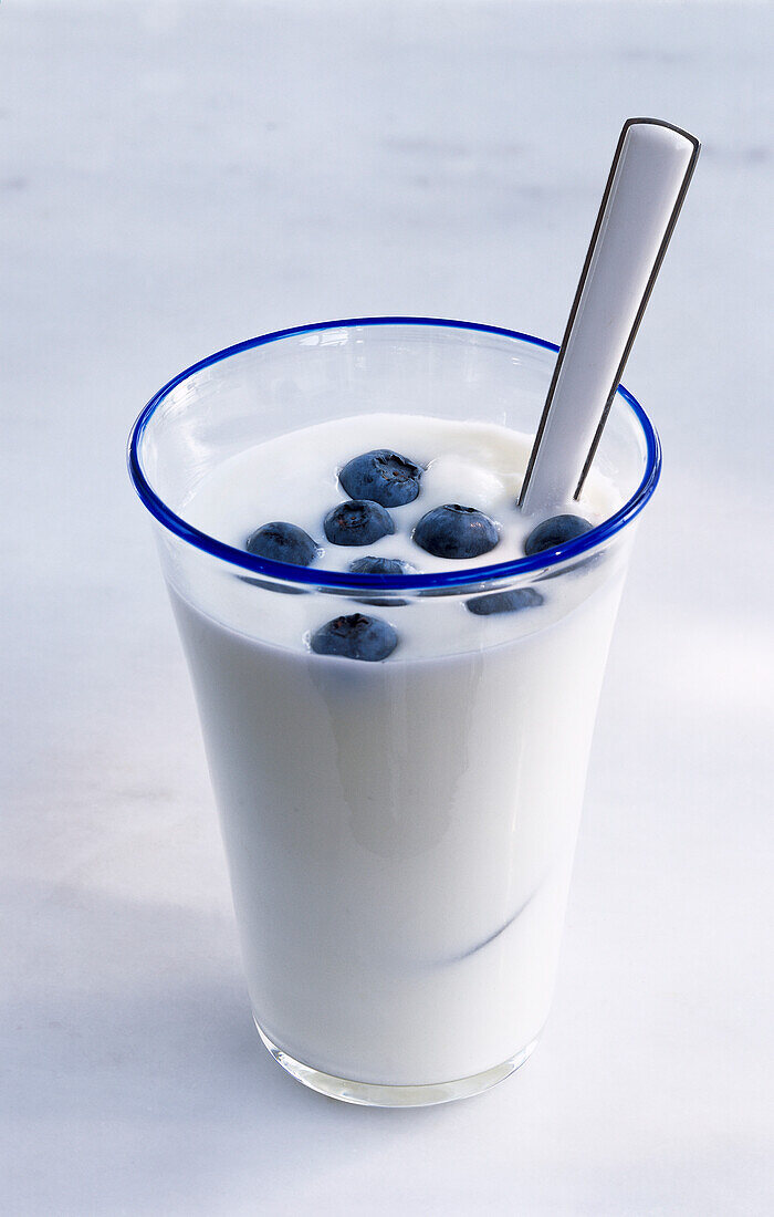 Ein Glas Joghurt mit einigen Blaubeeren und Löffel