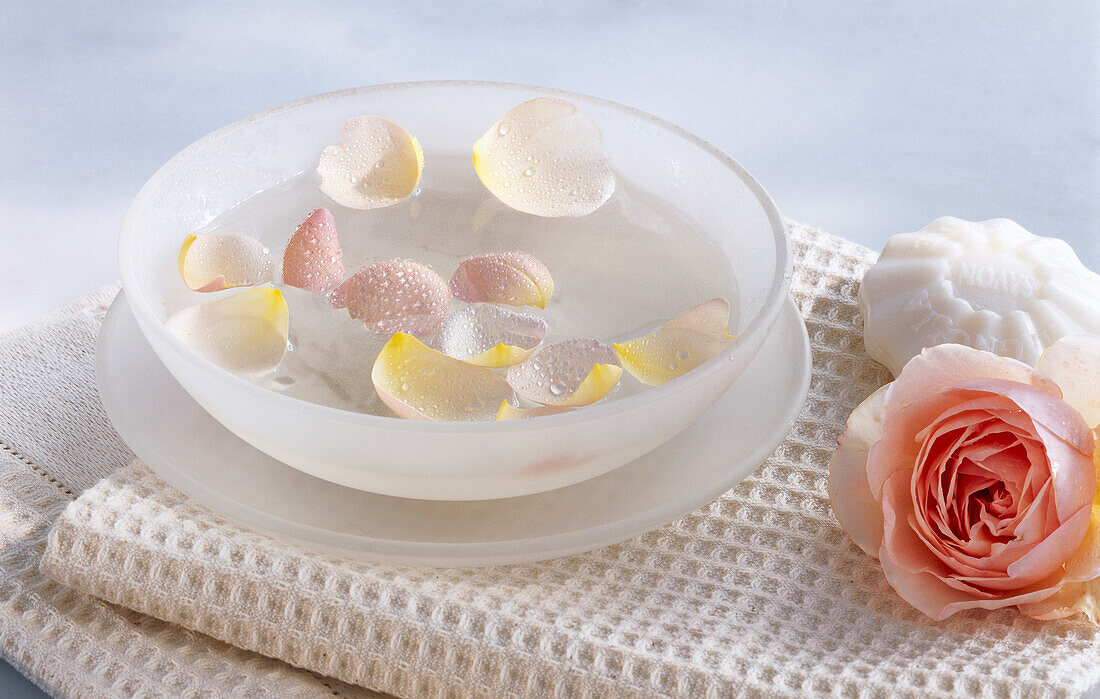 Rose petals in a bowl with water, on a towel with rose and soap
