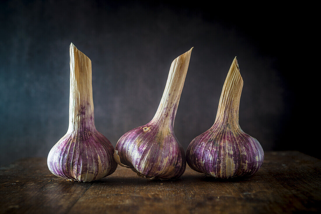 Drei frische, violette Knoblauchknollen auf Holztisch