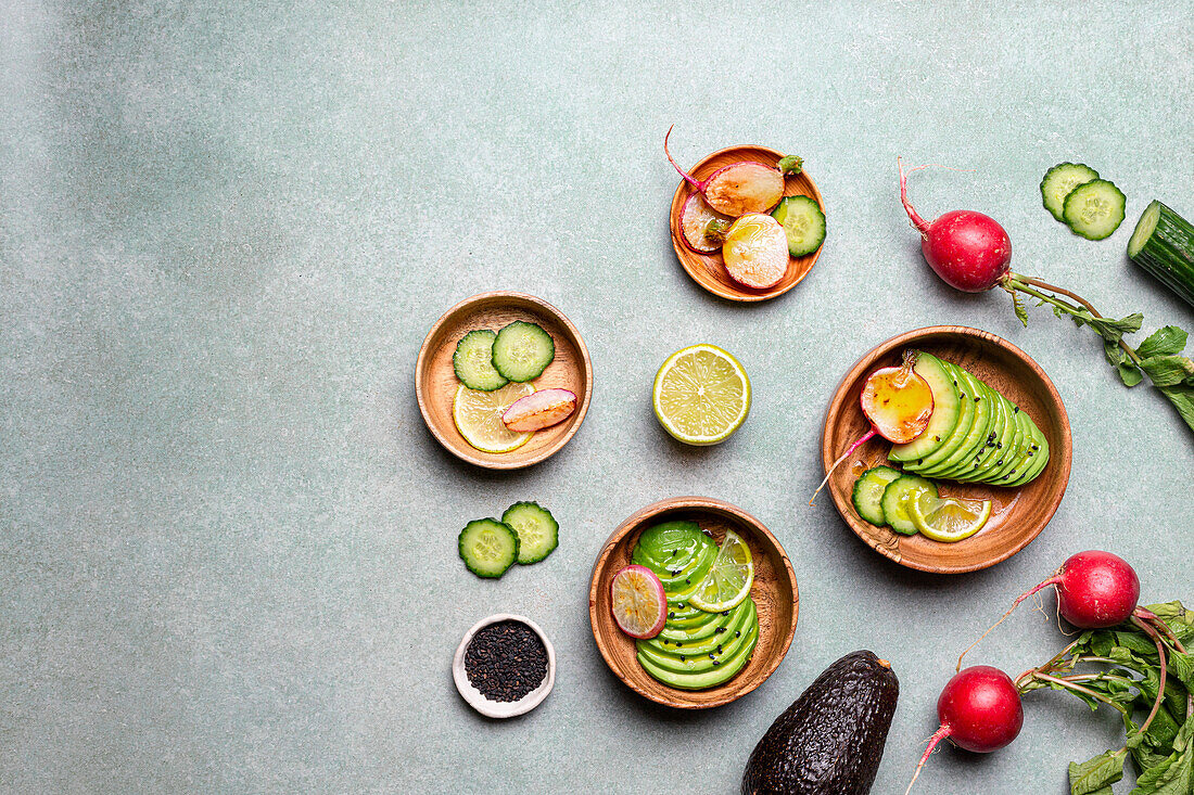 Assorted fresh vegetables and fruits arranged on plates - cucumber, lime, radish, avocado and chia seeds