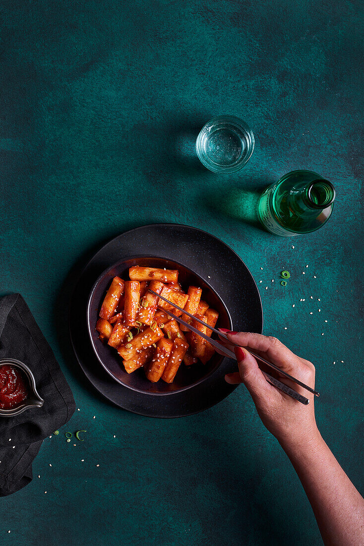 Eating traditional fried spicy tteokbokki in bowl on green background