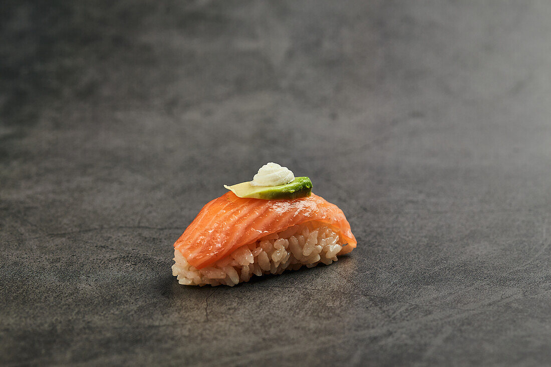 Nigiri sushi with slice of salmon on rice topped with thin slice of avocado and cream cheese