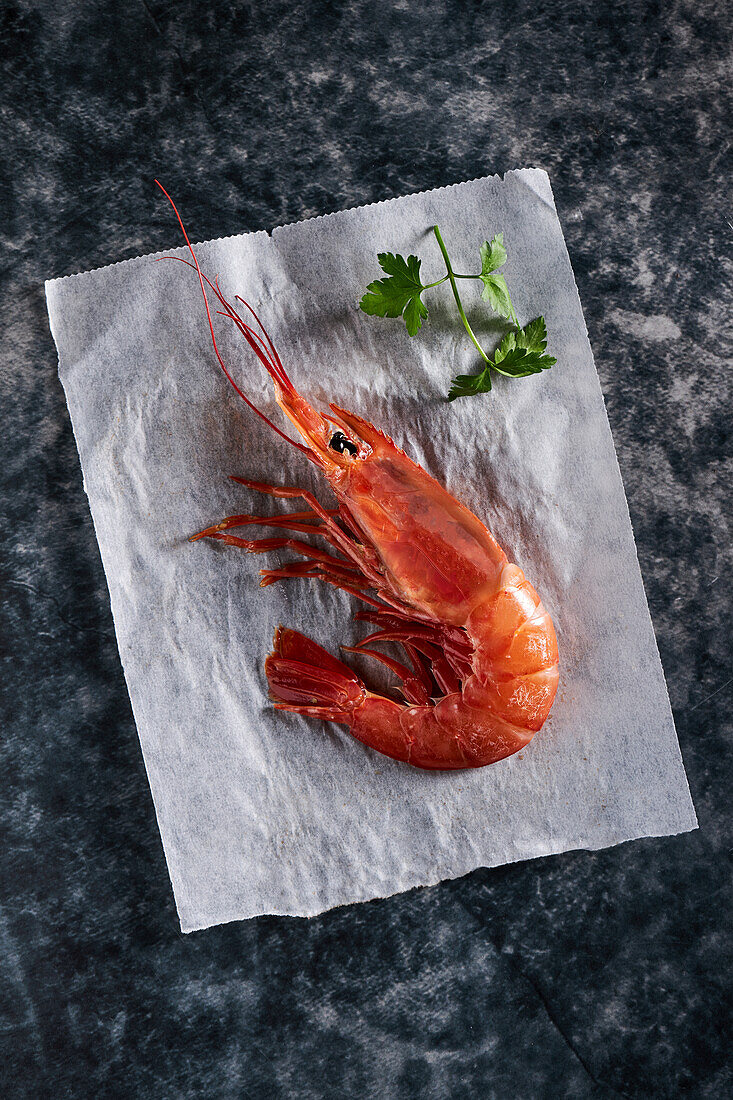 Shrimps in bowl with parsley placed on baking paper on dark marble surface table