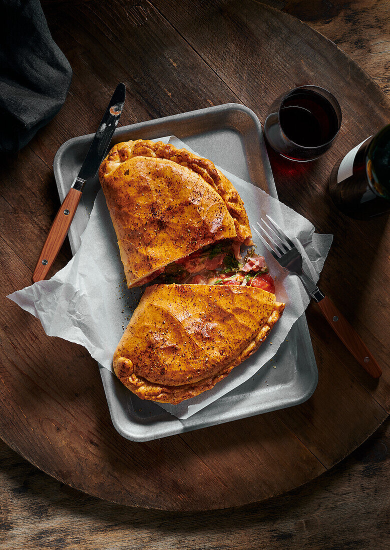 Pizza Calzone auf Pizzabrett daneben Glas und Flasche Rotwein