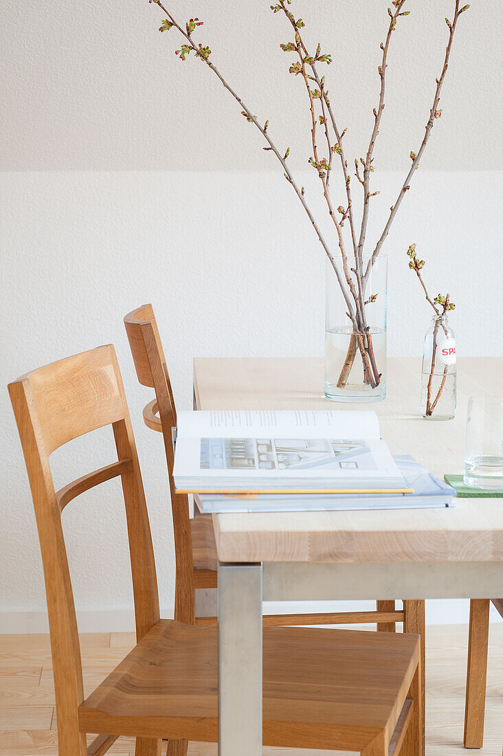 Buch und Frühlingszweige auf hellem Tisch mit Stühlen