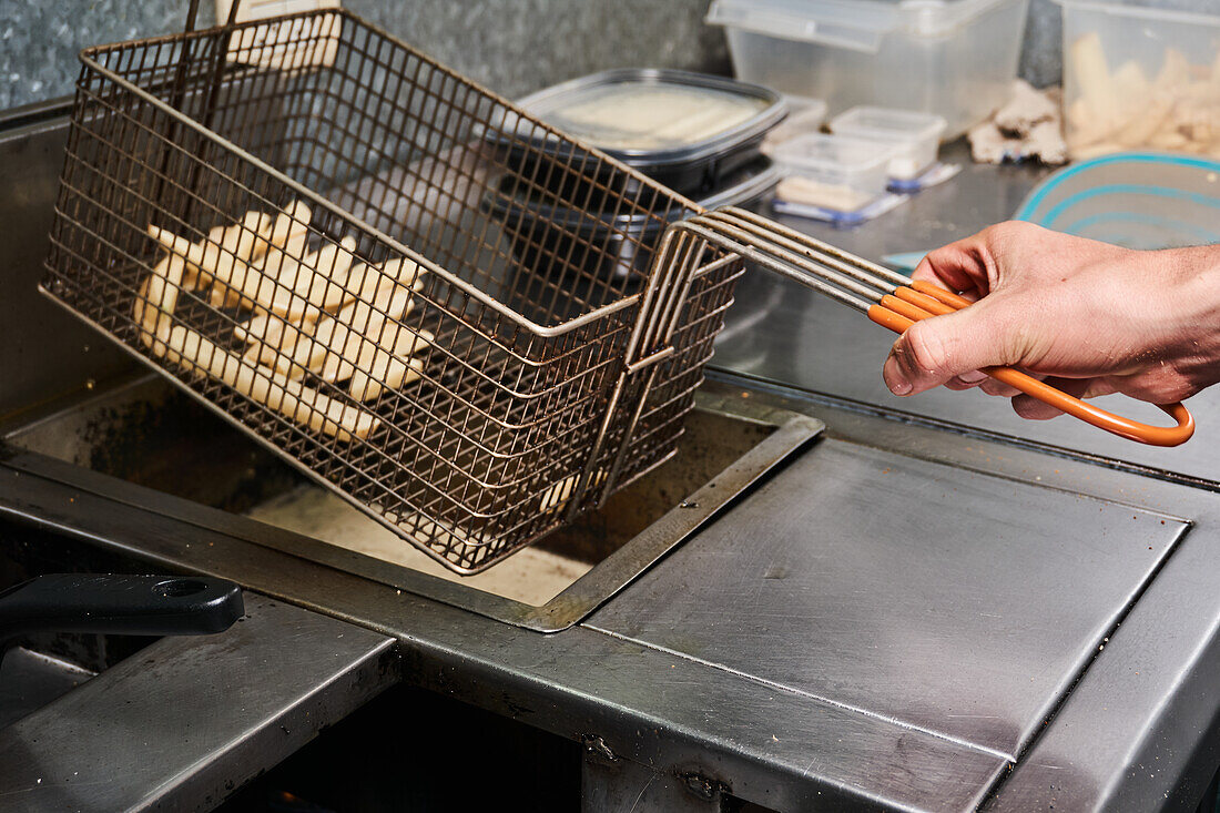 Side view of anonymous cook preparing French fries in deep fryer while working in restaurant kitchen