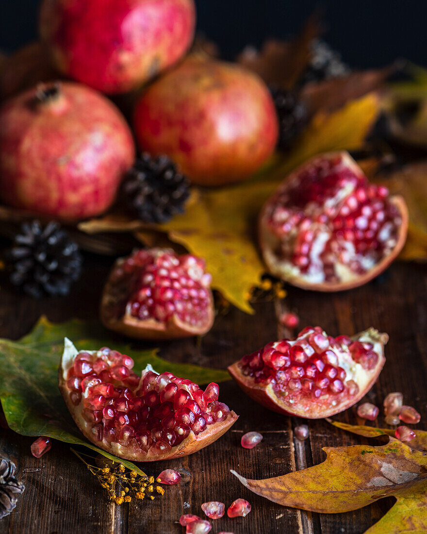 Parts of fresh red pomegranate placed on dark wooden table with autumn leaves