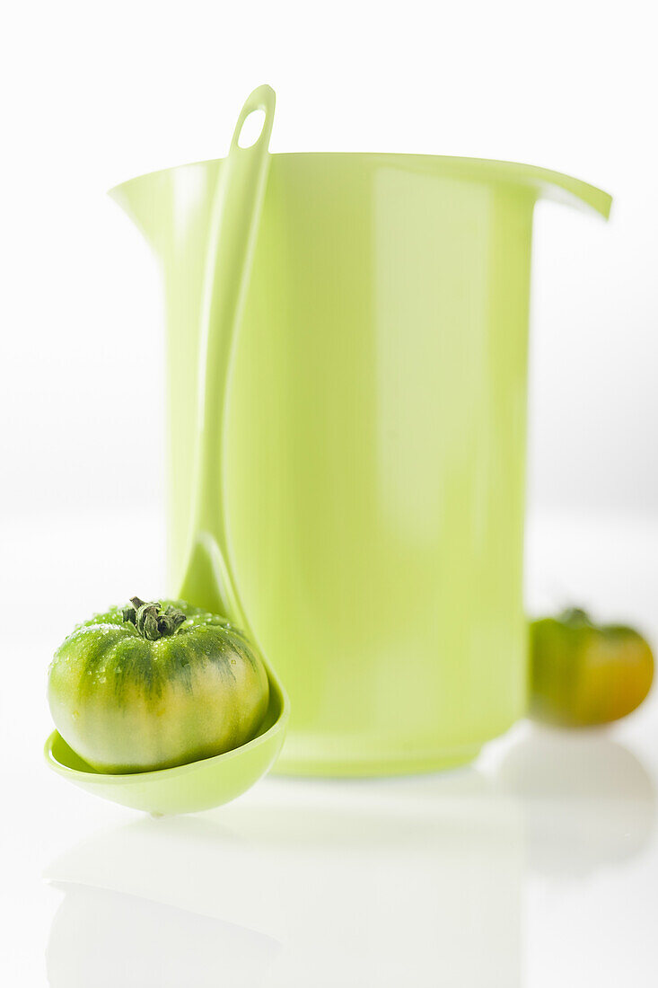 Green tomato in ladle in front of a green pitcher