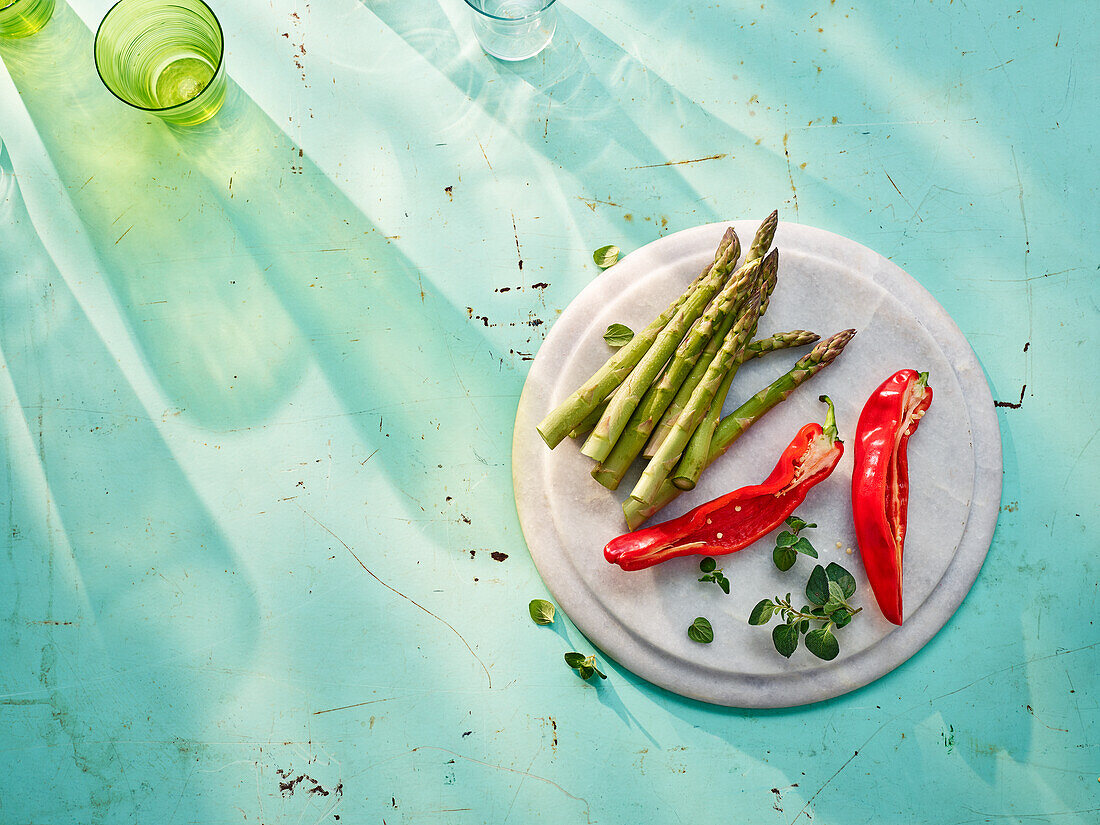 Grüner Spargel, rote Spitzpaprika und Majoran auf Schneidebrett