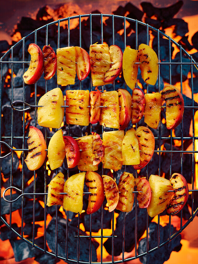 Mixed fruit skewers with orange zest and cinnamon on the grill