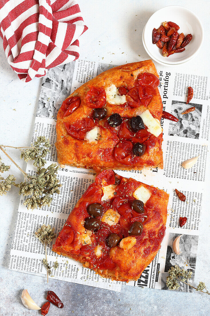 Pizza mit Mozzarella, Tomaten und Oliven auf Zeitungspapier