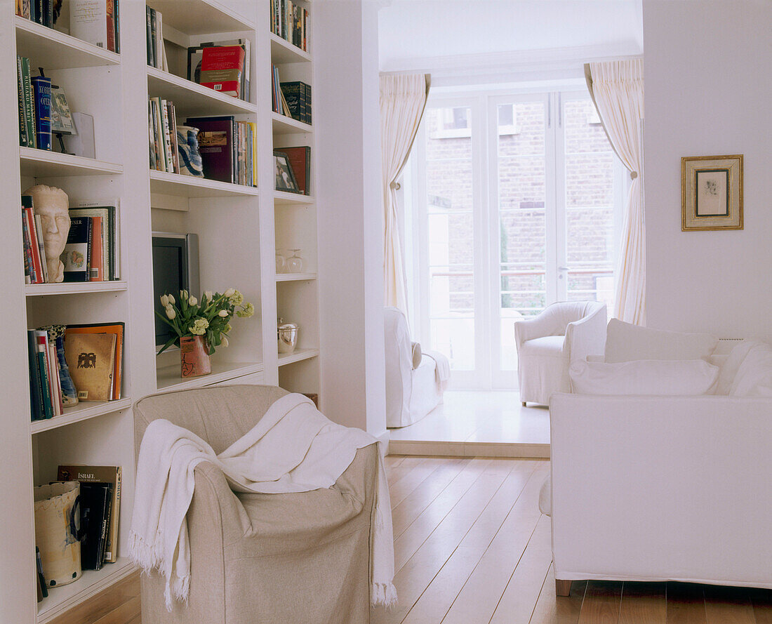 A traditional living room decorated in neutral colours upholstered sofa covered seat built in shelving painted floorboards window