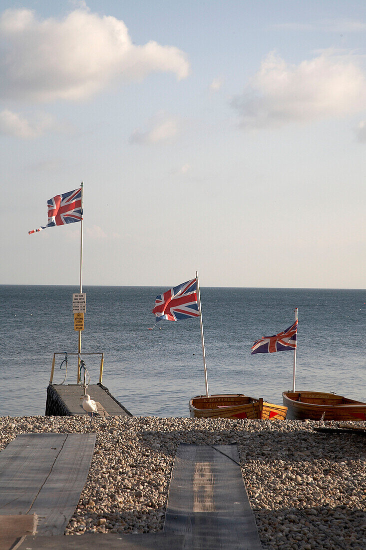 Union Jacks fly on rowing boats moored on Devon shingle