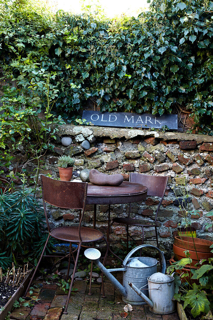 Rusty metal garden table and chairs with watering cans in Brighton garden, Sussex, UK