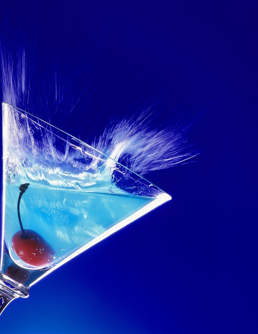 Blauer Curacao-Cocktail schwappt aus Martiniglas