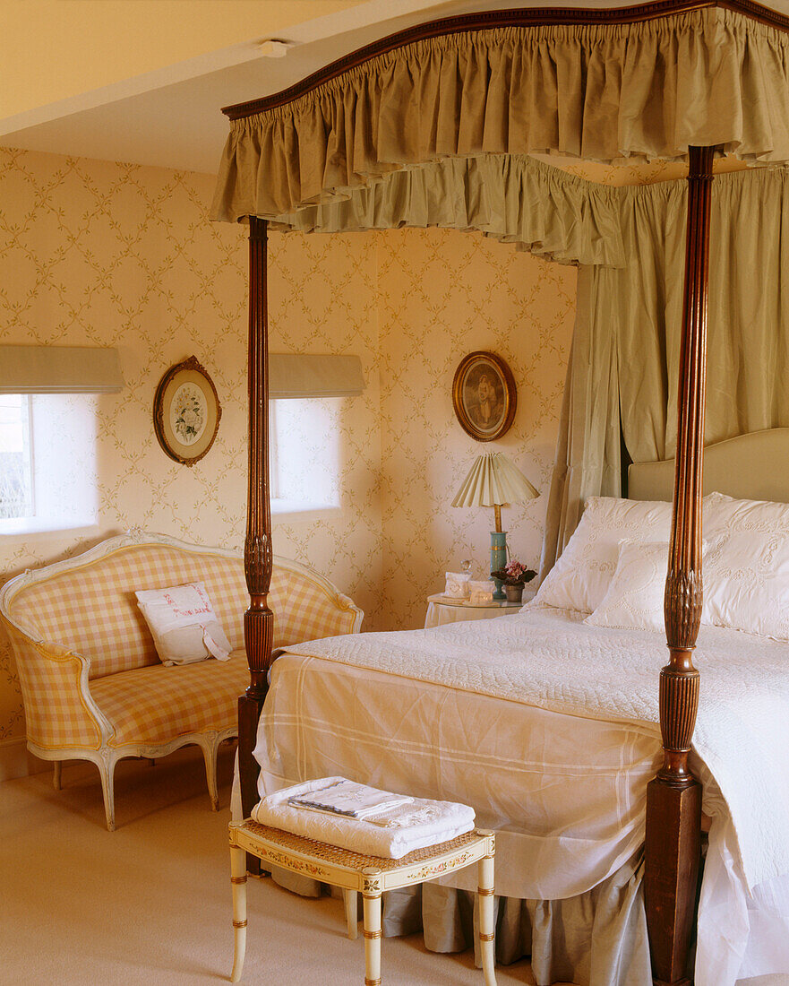 Traditionelles gelbes Schlafzimmer mit Mustertapete, Himmelbett, Polstersofa, Nachttisch und Hocker