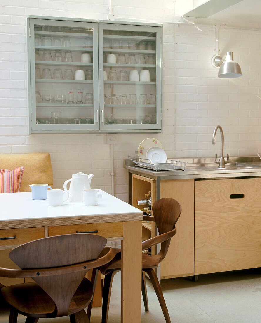 A modern kitchen dining table and kitchen work top with a glass display cabinet full of glasses in0between