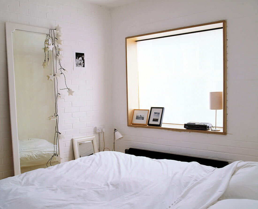 A modern bedroom with a large square window illuminating the bed with a large full length mirror opposite it