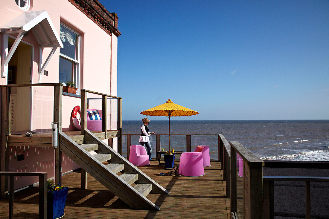 Frau auf der Balkonterrasse eines Strandhauses in Cromer, Norfolk, UK