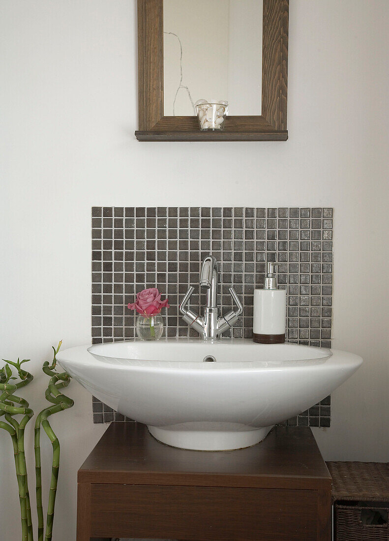 Detail of modern bathroom with white sink on a wooden base and framed mirror above