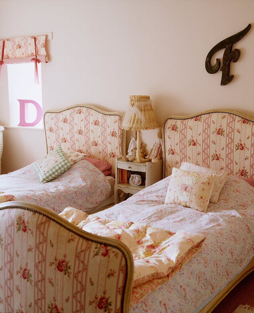 A traditional guest bedroom twin single beds with upholstered head and foot boards floral pattern fabric bedside table lamp cushions