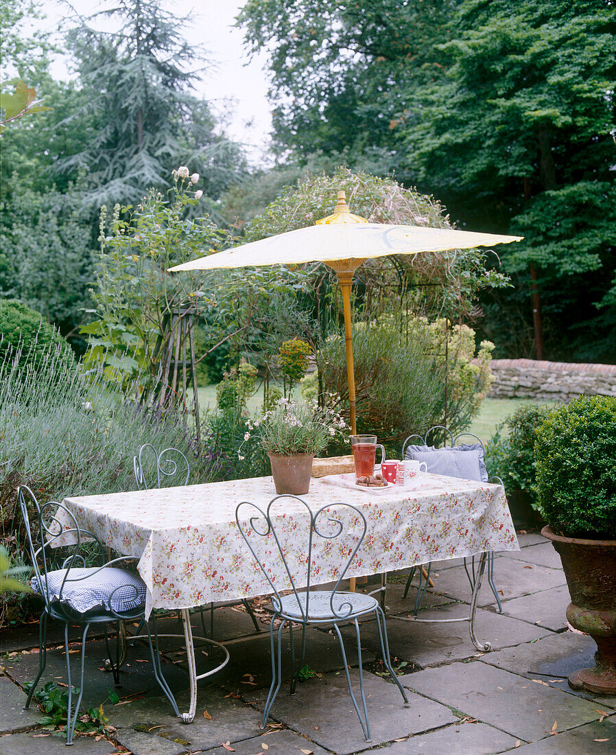 Gartentisch mit schmiedeeisernen Stühlen und Sonnenschirm auf gepflastertem Terrassenplatz