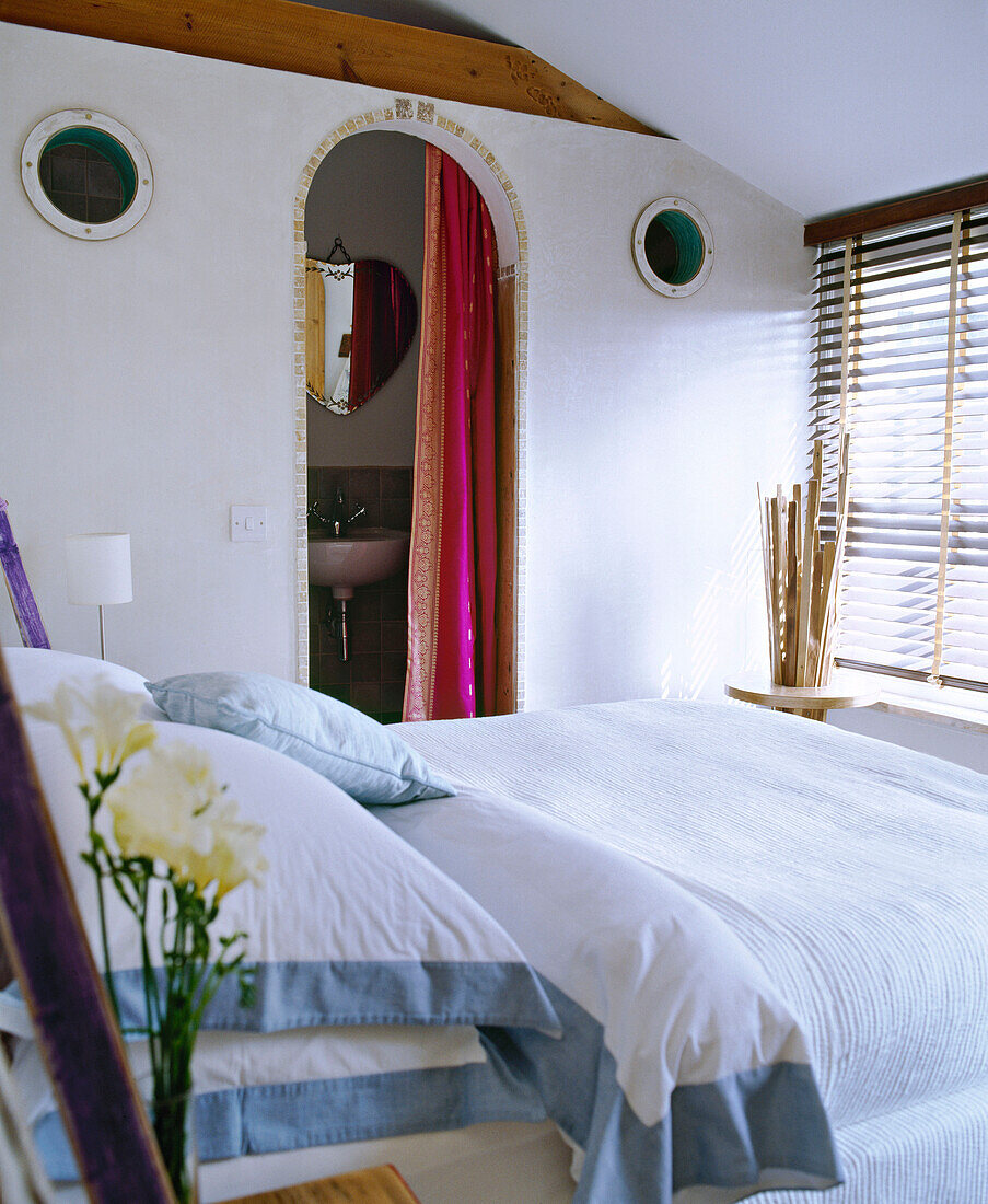 Doppelbett in einem weißen Schlafzimmer mit Türbogen zum eigenen Bad