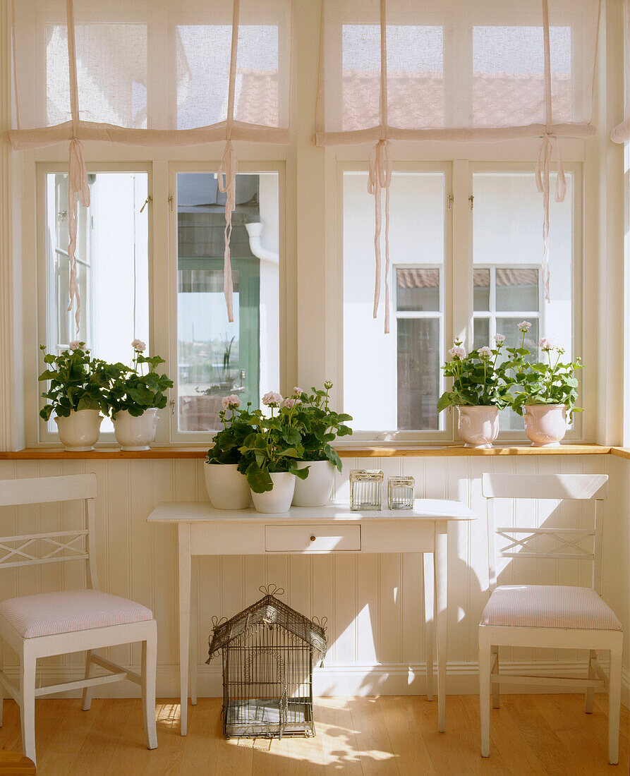 A detail of a country style living room done in neutral colours with side table chairs and plants on the table and windowsill